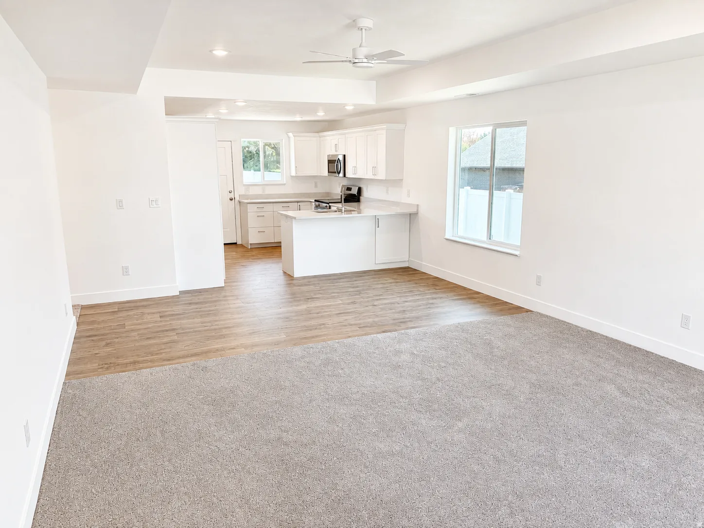 Open-concept living space with light gray carpeting and wood-finish flooring