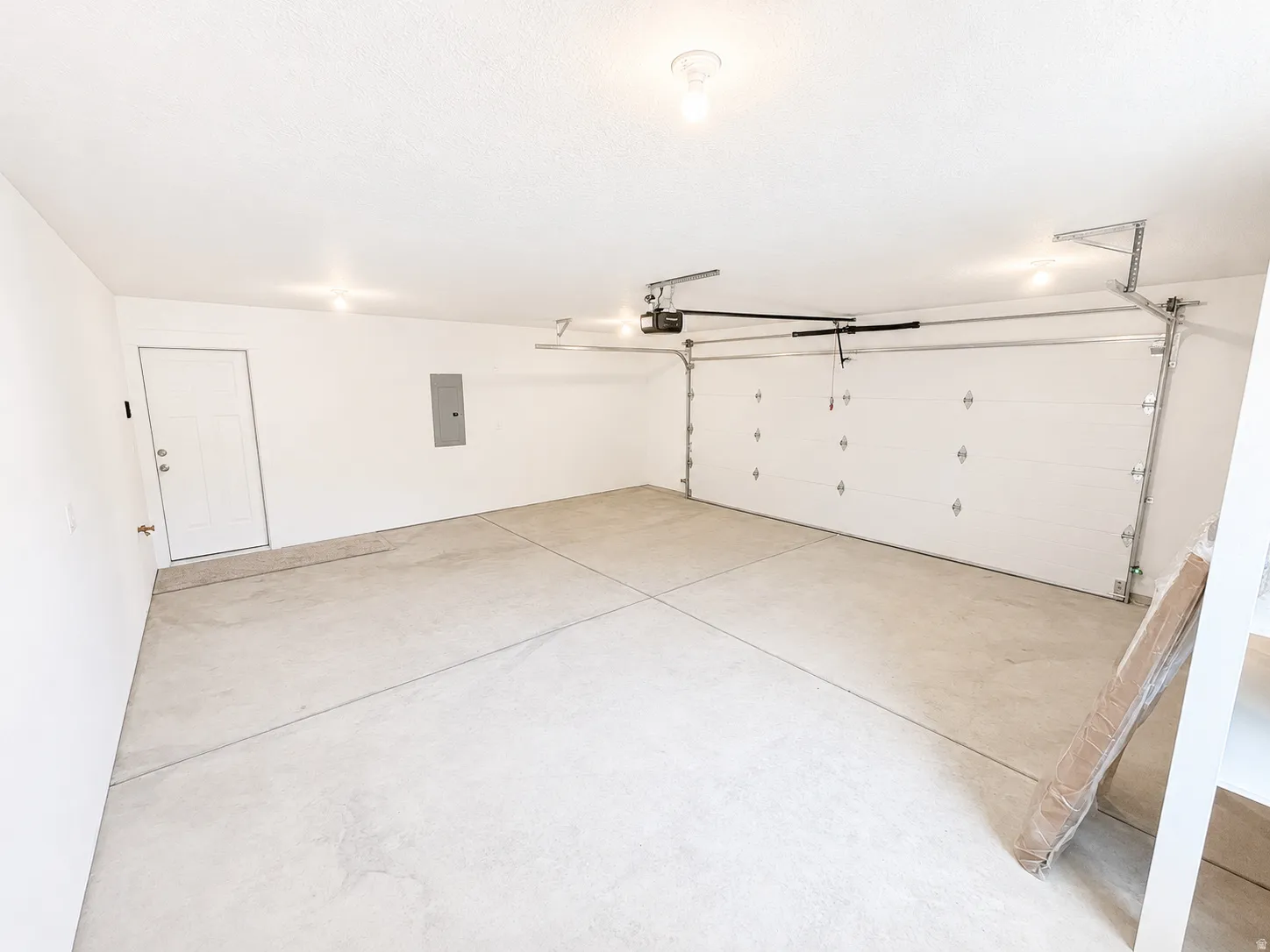 Spacious two-car garage featuring a white paneled door, concrete flooring, and recessed lighting