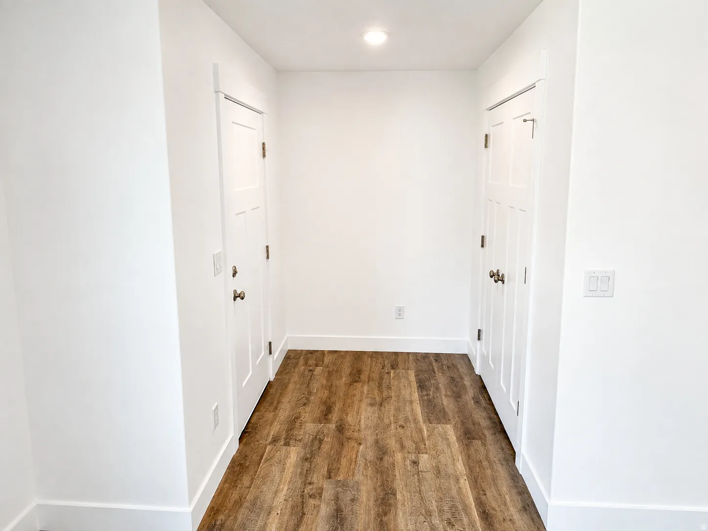 Hallway featuring wood-finish flooring, white paneled doors, recessed ceiling lighting, and crisp white baseboards
