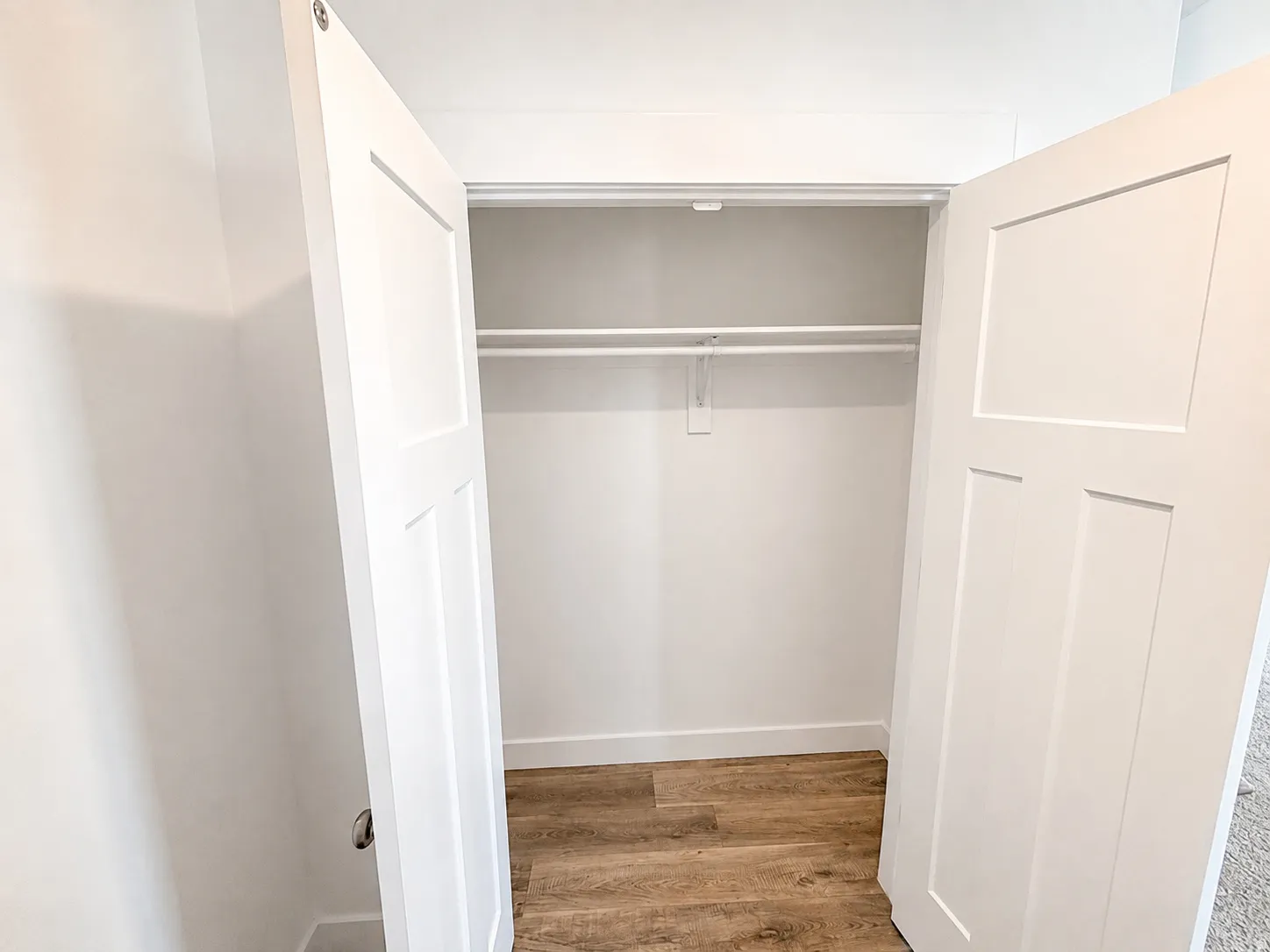 White paneled bi-fold closet doors revealing a storage area with wood-finish flooring and white shelving and hanging rods