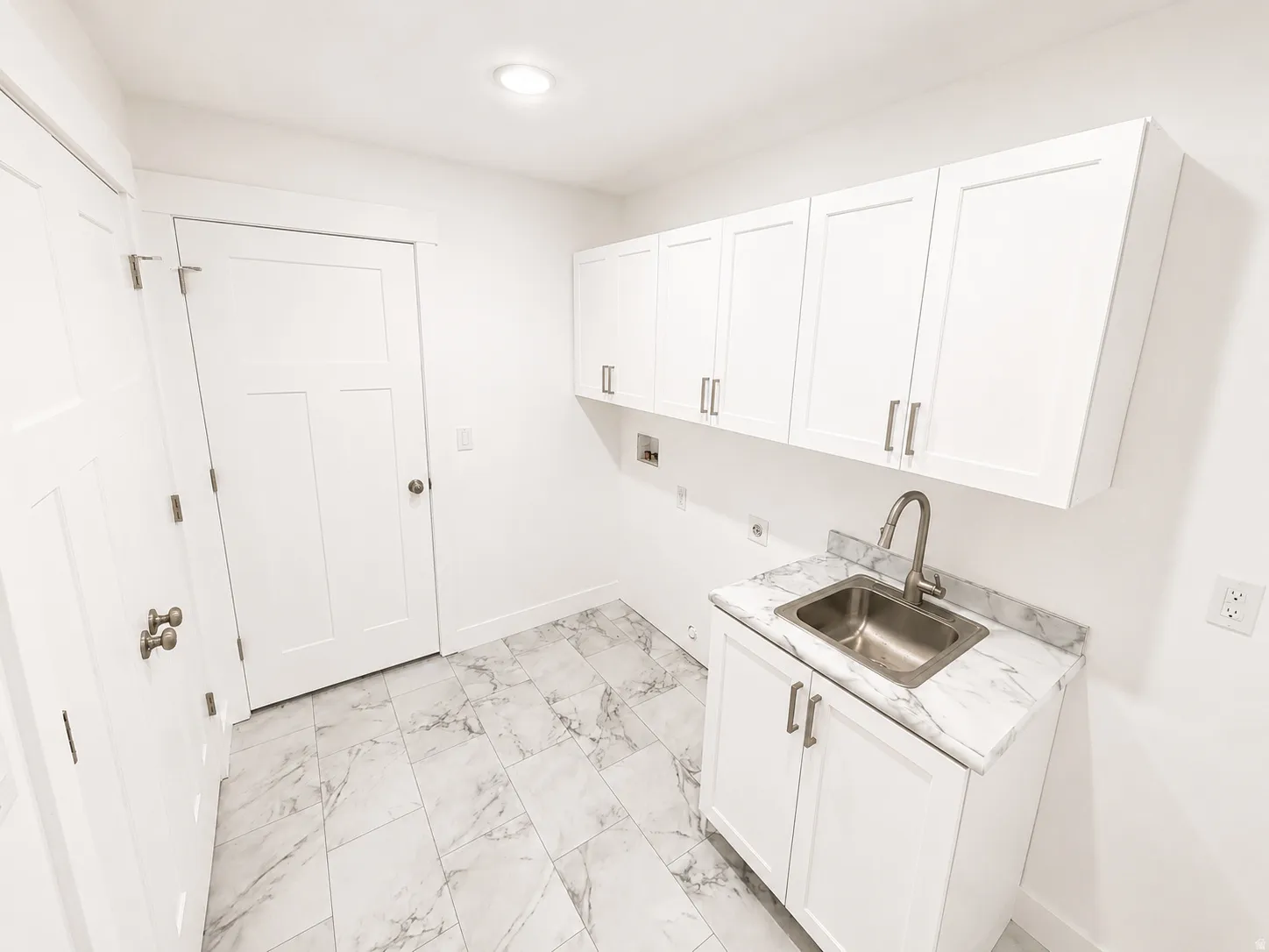 Bright utility space featuring white cabinetry, a stainless steel sink with a high-arc faucet, and a white countertop with grey veining