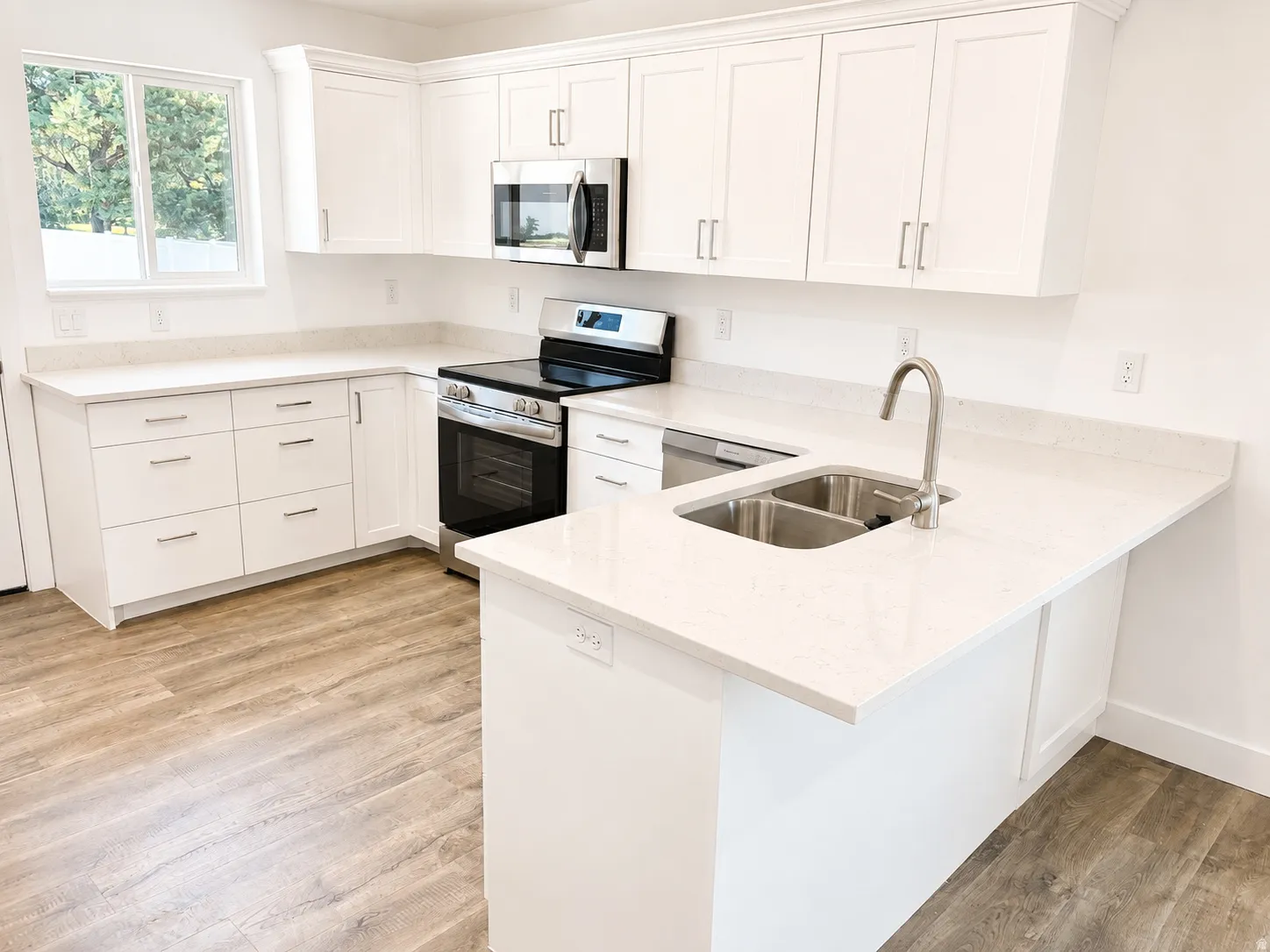 Contemporary kitchen featuring white cabinetry, light-toned countertops, stainless steel appliances, a dual basin sink with a gooseneck faucet, and wood-finish flooring