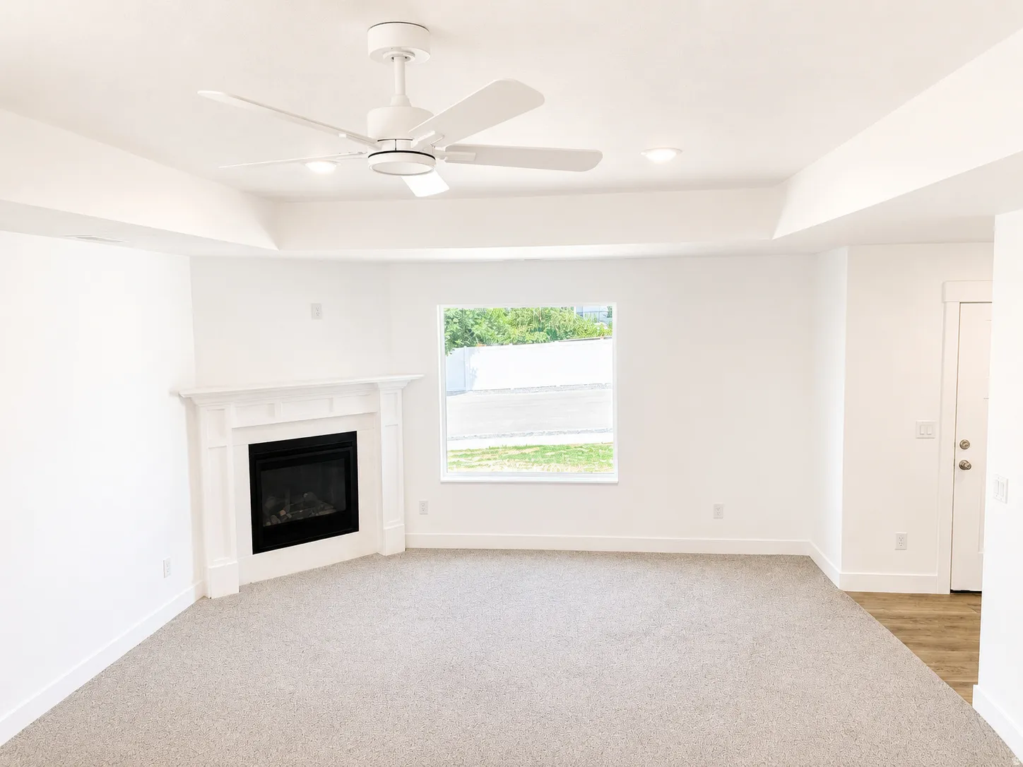 Living area featuring a corner fireplace with a white mantel, tray ceiling, and a ceiling fan with integrated lighting