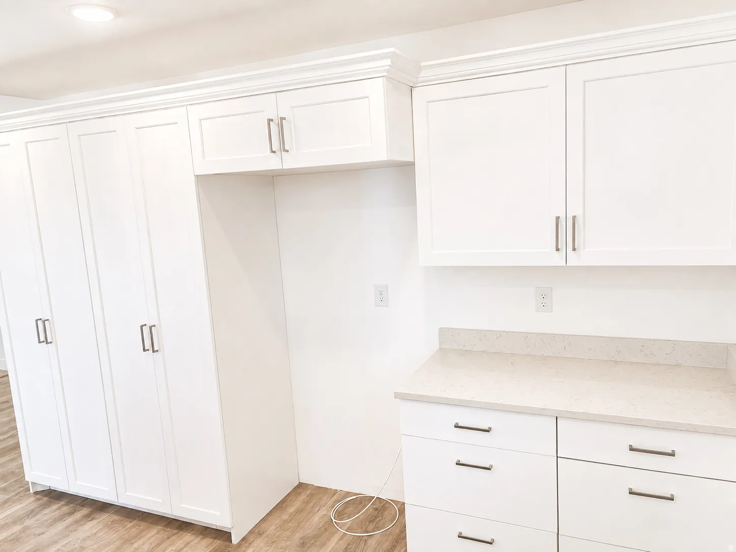 Crisp white cabinetry with brushed nickel hardware, light-toned countertops, wood-finish flooring, and crown molding accents