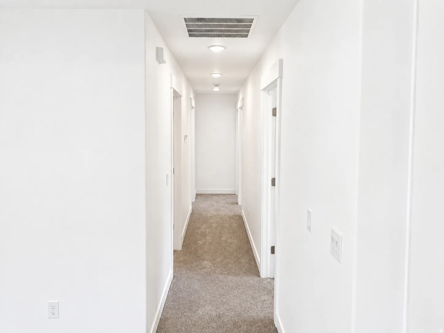 Hallway with light gray carpeting, crisp white walls, recessed lighting, white trim, and doors with dark hardware