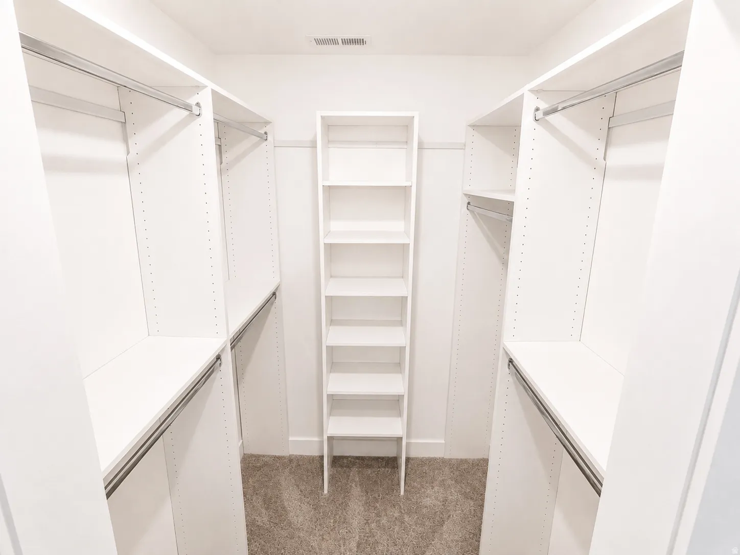 Master Walk-in closet featuring white built-in shelving, multiple hanging rods, and a central freestanding shelving unit over carpeted flooring