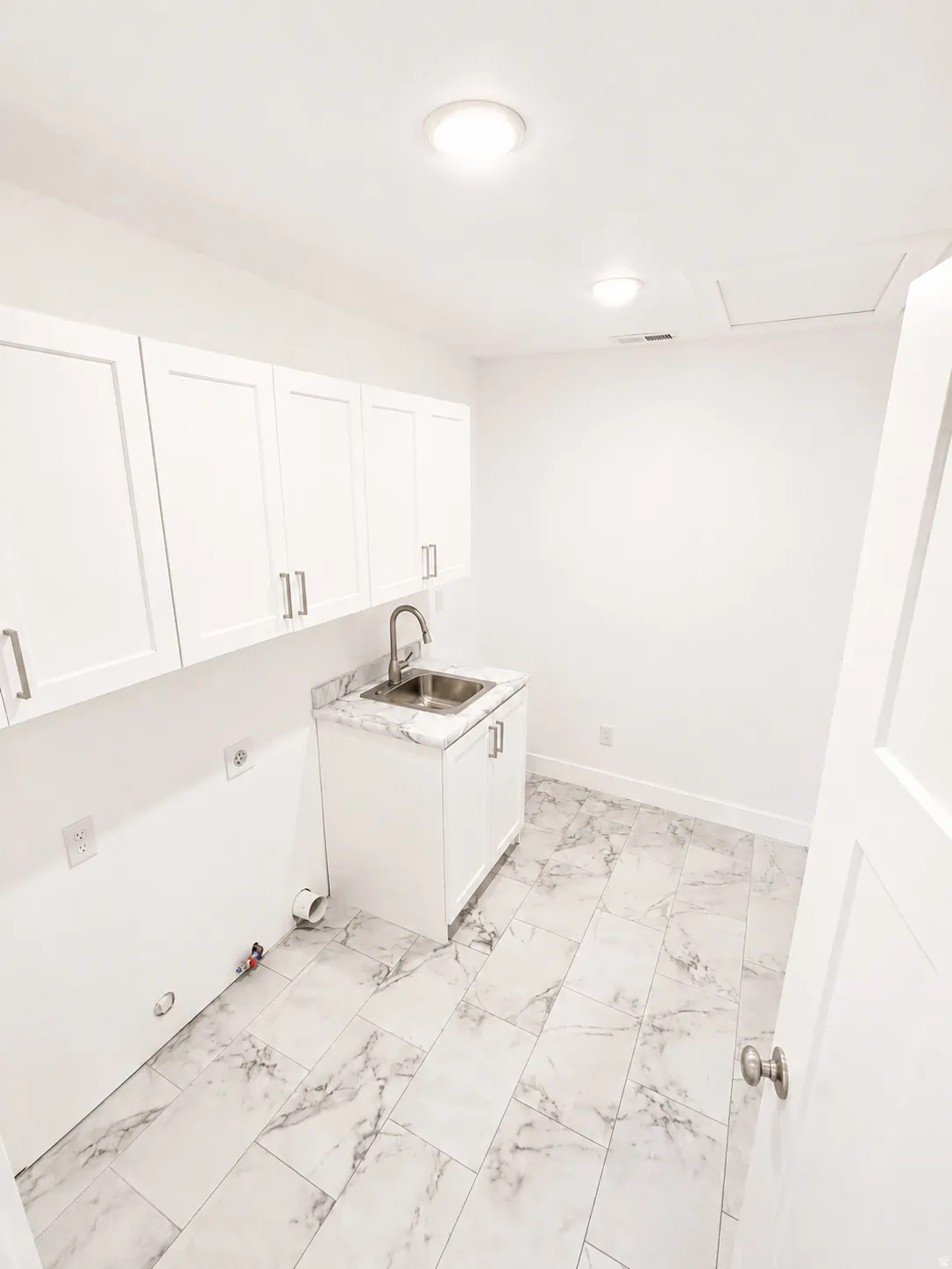Utility room featuring white shaker cabinetry, a stainless steel sink with a gooseneck faucet, a white countertop with a gray veining pattern, and light-toned rectangular floor tiles