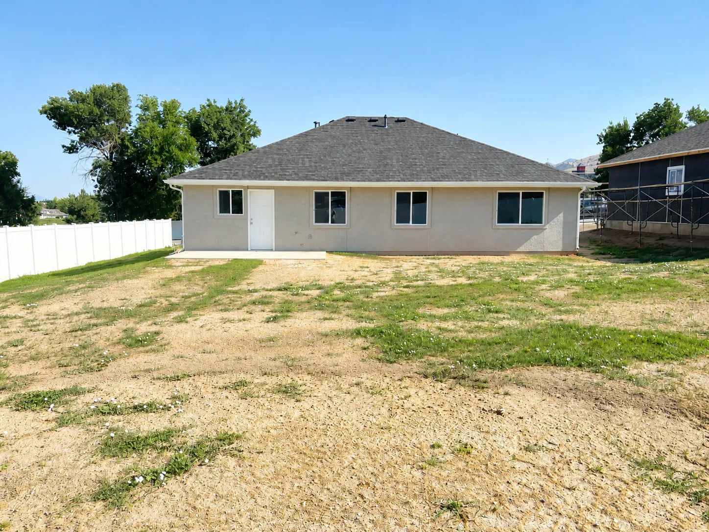Rear exterior featuring a stucco finish, dark shingle roof, and multiple windows