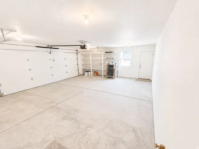 Spacious garage featuring a two-car overhead door with opener, concrete flooring, built-in shelving, and a side entry door with an opaque window