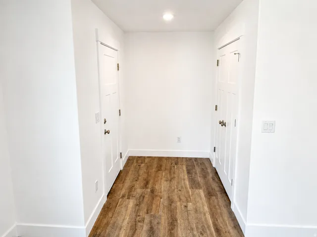 Hallway featuring wood-finish flooring, white paneled doors, recessed ceiling lighting, and crisp white baseboards