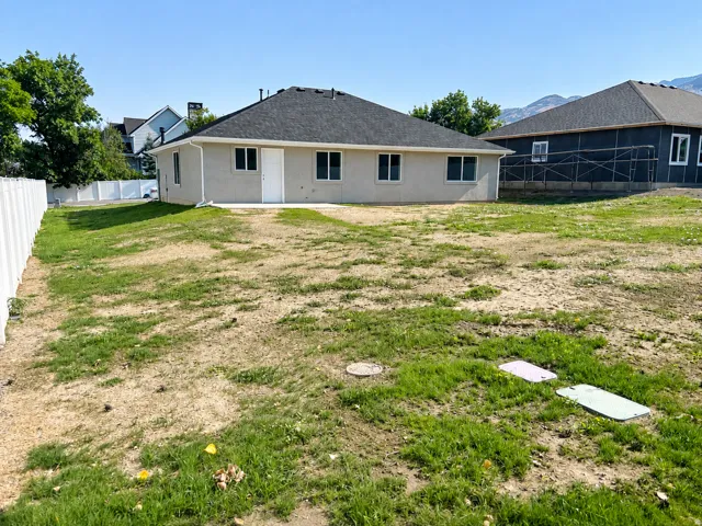 Rear exterior featuring a stucco finish, dark shingle roof, and multiple windows