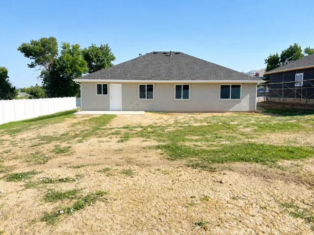 Rear exterior featuring a stucco finish, dark shingle roof, and multiple windows