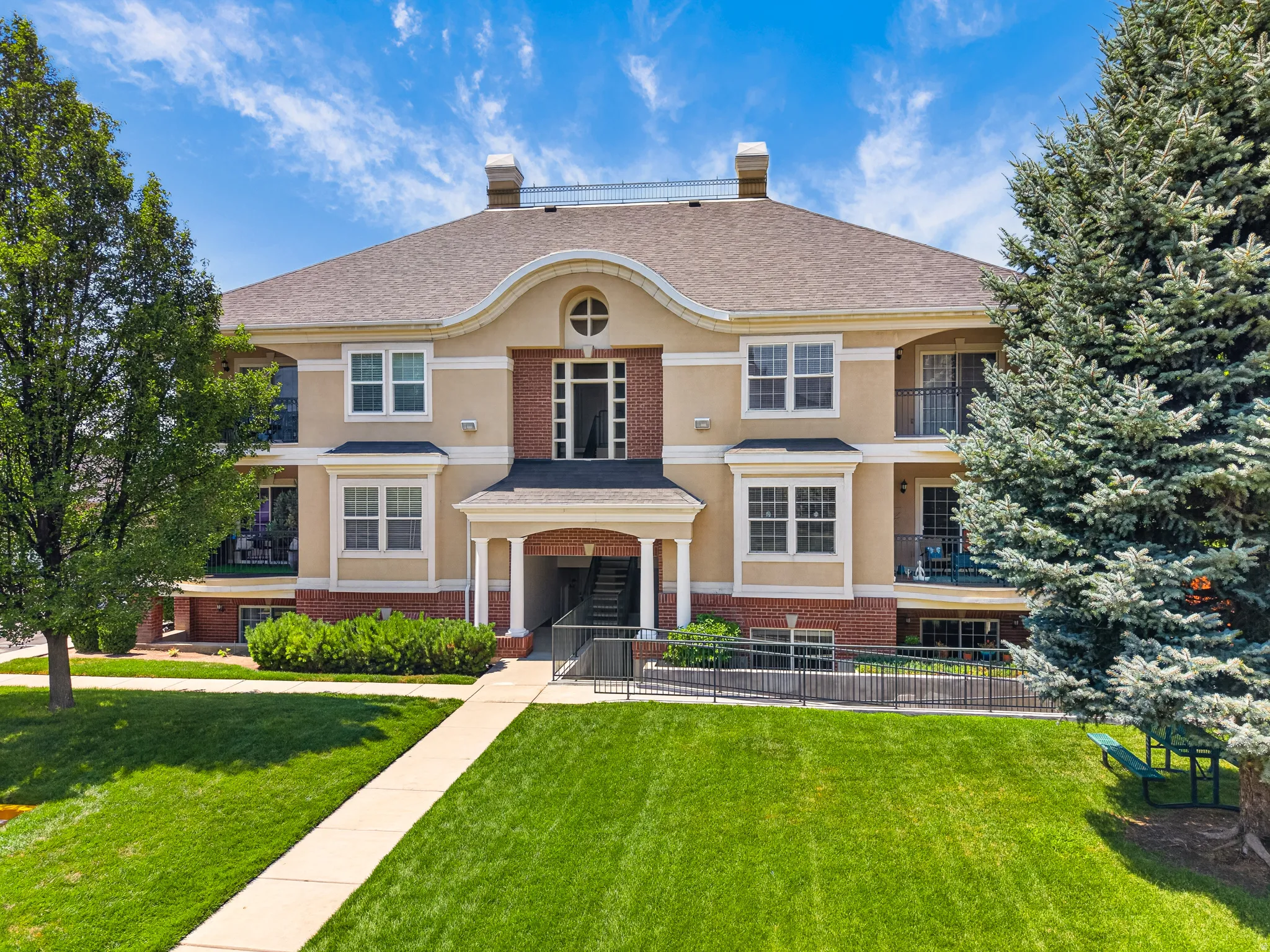 Elegant two-story Colonial residence featuring a cream and brick exterior with symmetrical architecture, arched entry portico with dark wood doors, and multiple multi-pane windows