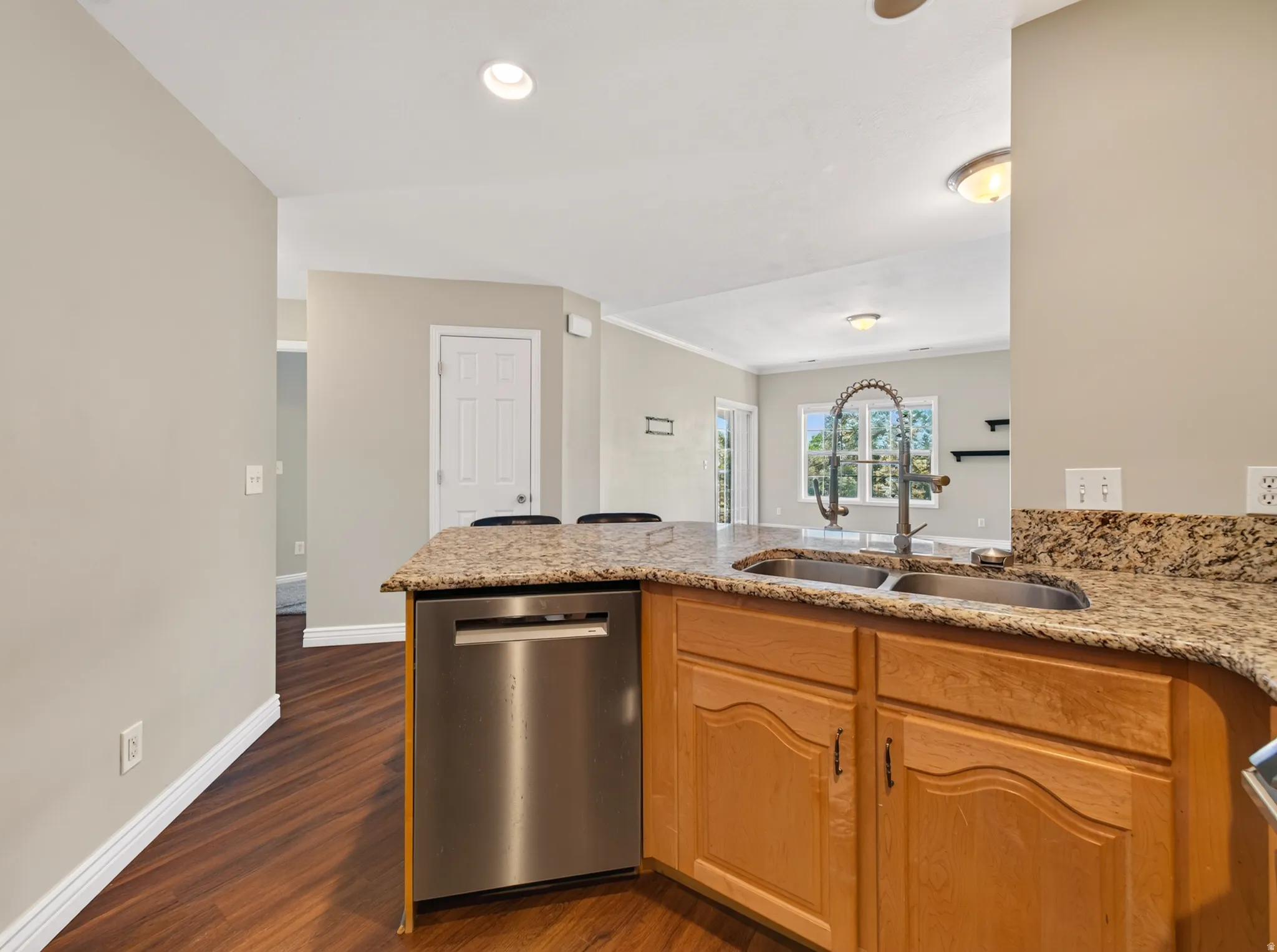 Kitchen island with a double basin sink and gooseneck faucet, light-toned wood cabinetry, granite countertops, and a stainless steel dishwasher