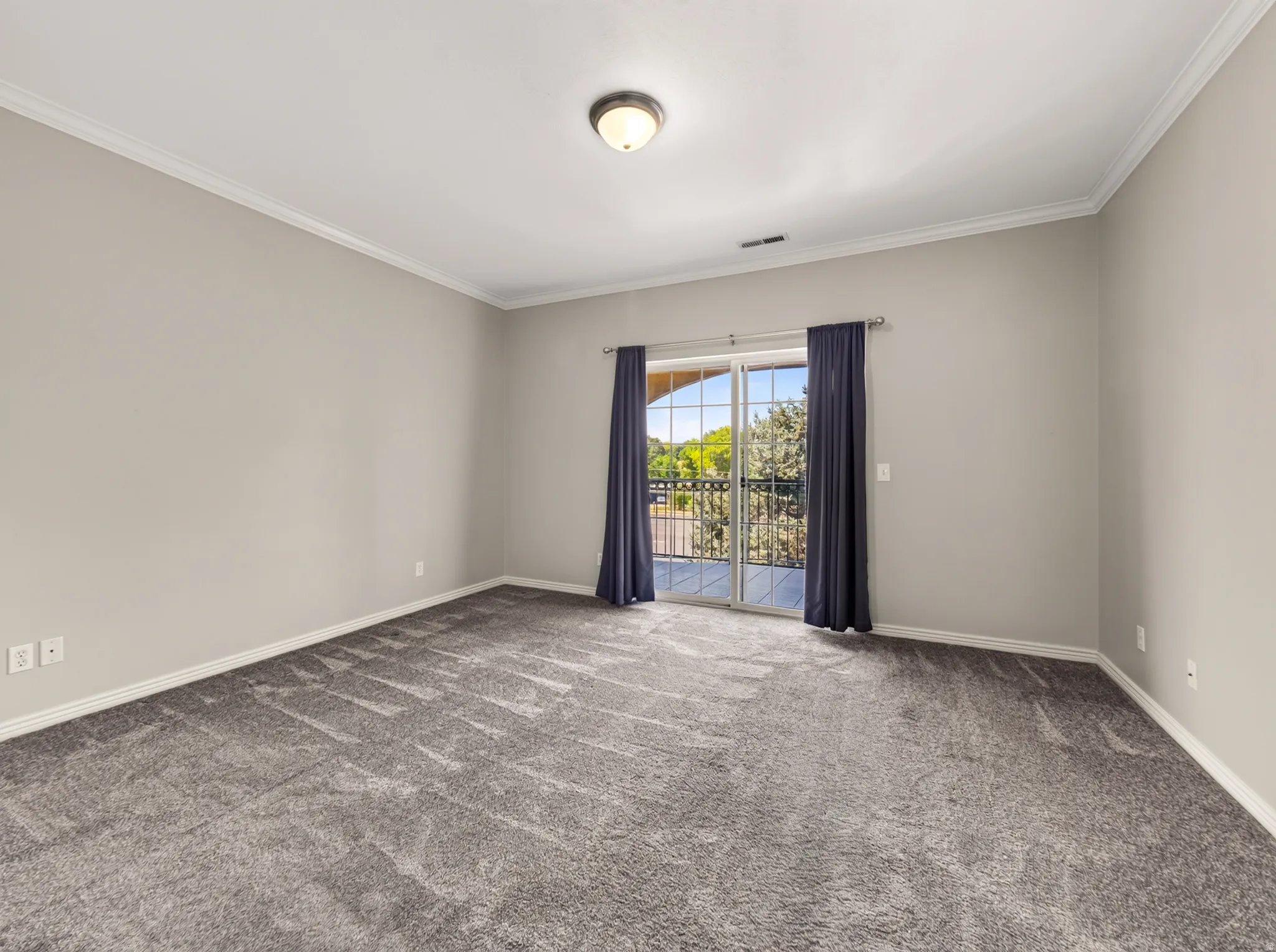 Spacious interior featuring a sliding glass door, crown molding, baseboards, recessed ceiling light, and gray carpeting