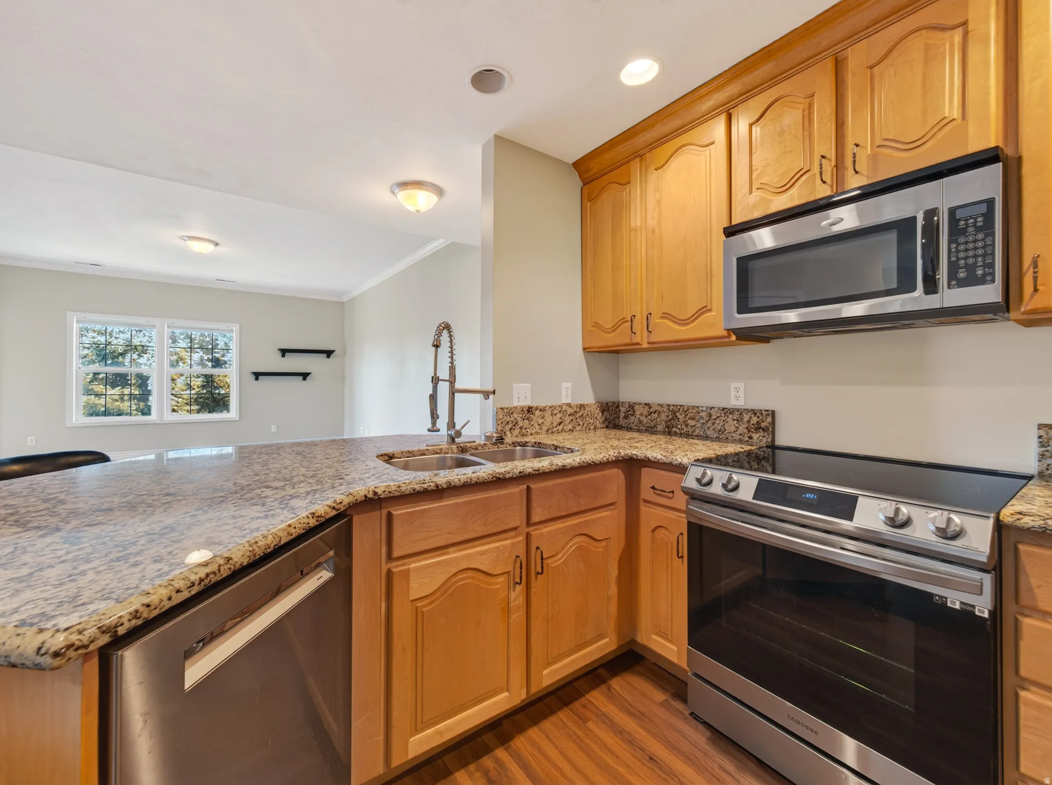 Kitchen featuring light wood cabinetry, granite-style countertops, stainless steel appliances, and wood-finish flooring