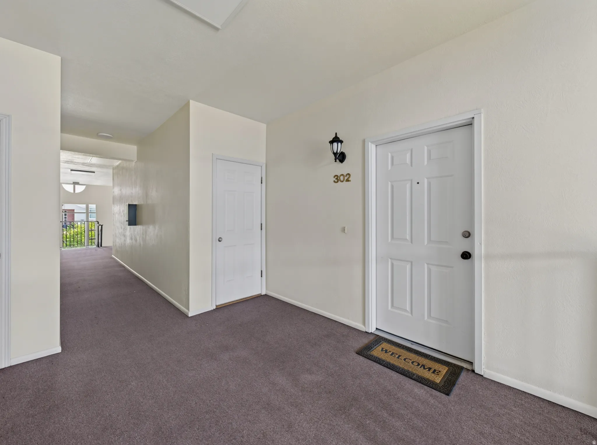 Entryway featuring a paneled door with a brass kickplate, a wall-mounted light fixture, and neutral-toned carpeting