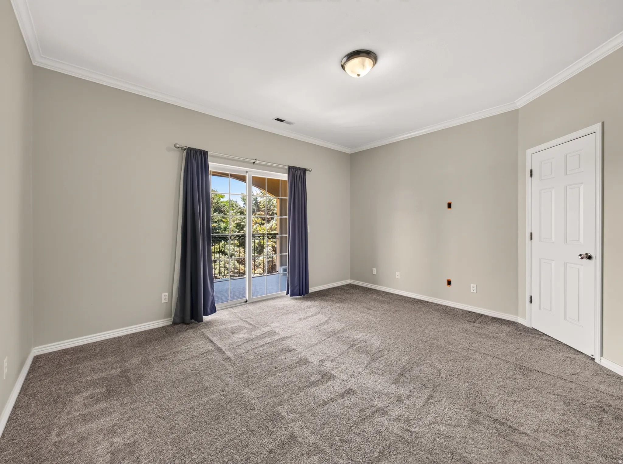 Spacious room featuring neutral wall tones, gray carpeting, white crown molding, and a sliding glass door