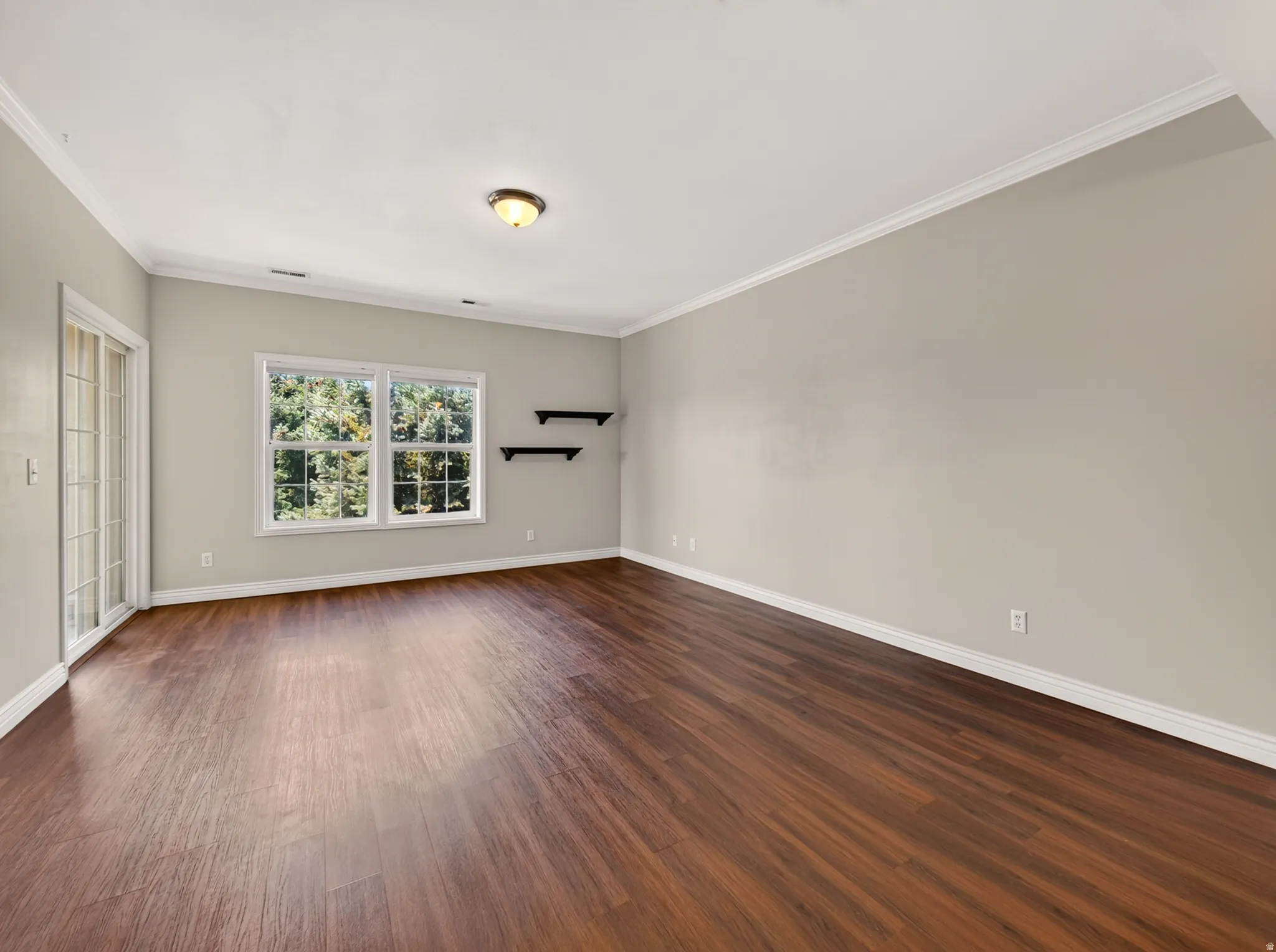 Spacious room featuring rich wood-finish flooring, light neutral-toned walls, and white crown molding