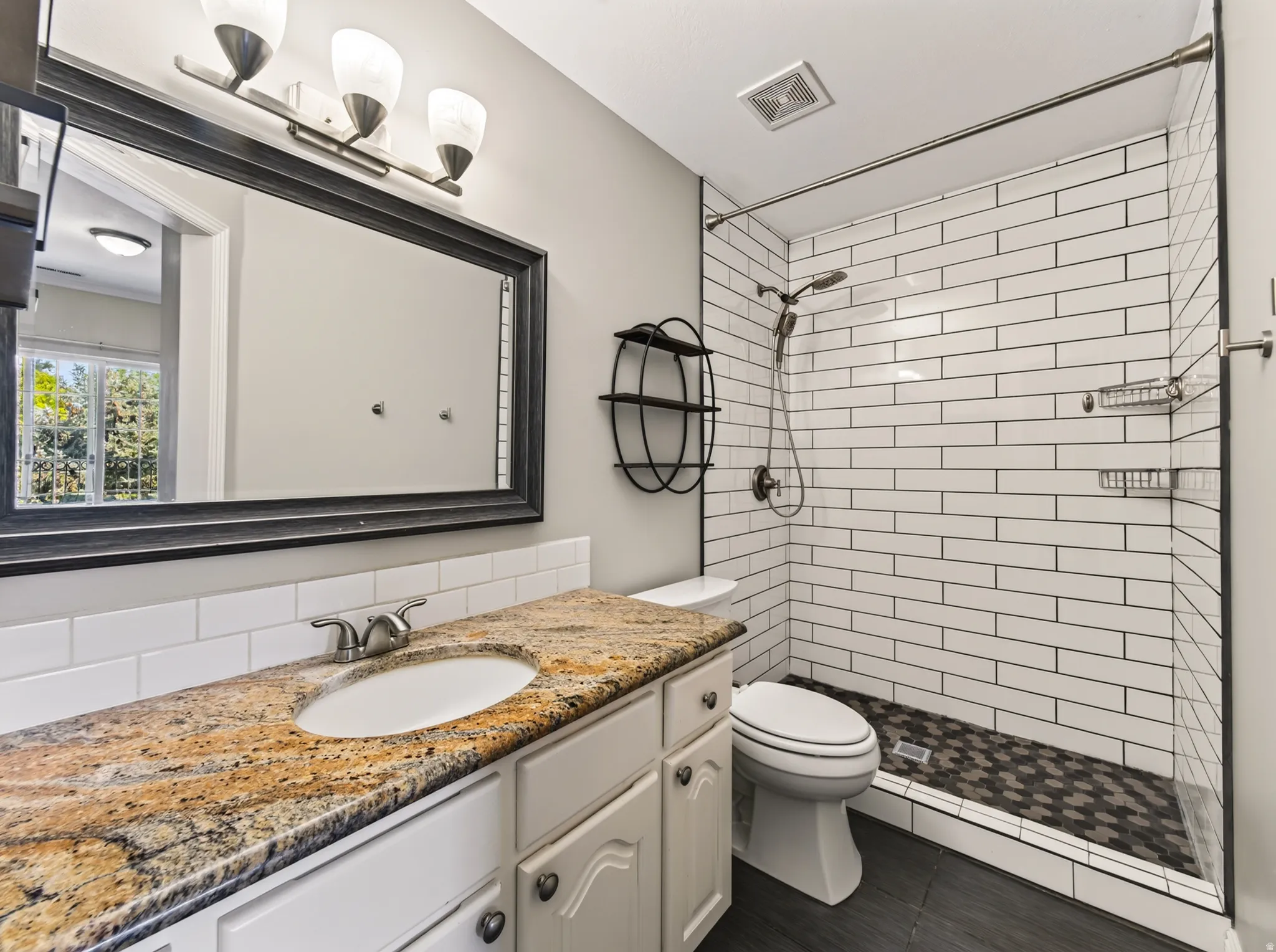 Bathroom featuring a granite-style countertop vanity with a white subway tile backsplash, a glass-enclosed shower with white subway tile walls, and a hexagonal tile shower floor