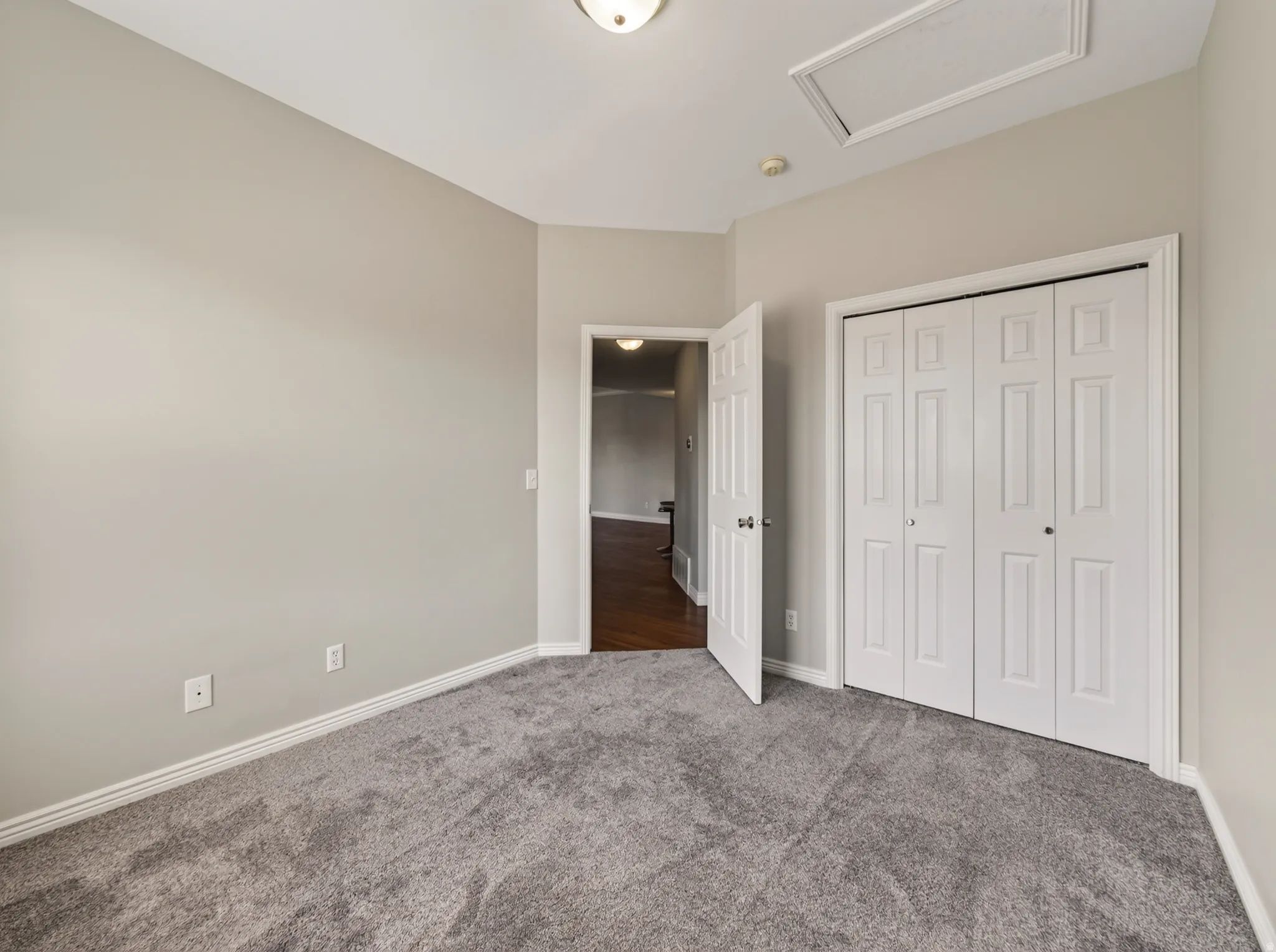 Neutral-toned room featuring light gray carpeting, white baseboards, and a white bi-fold closet