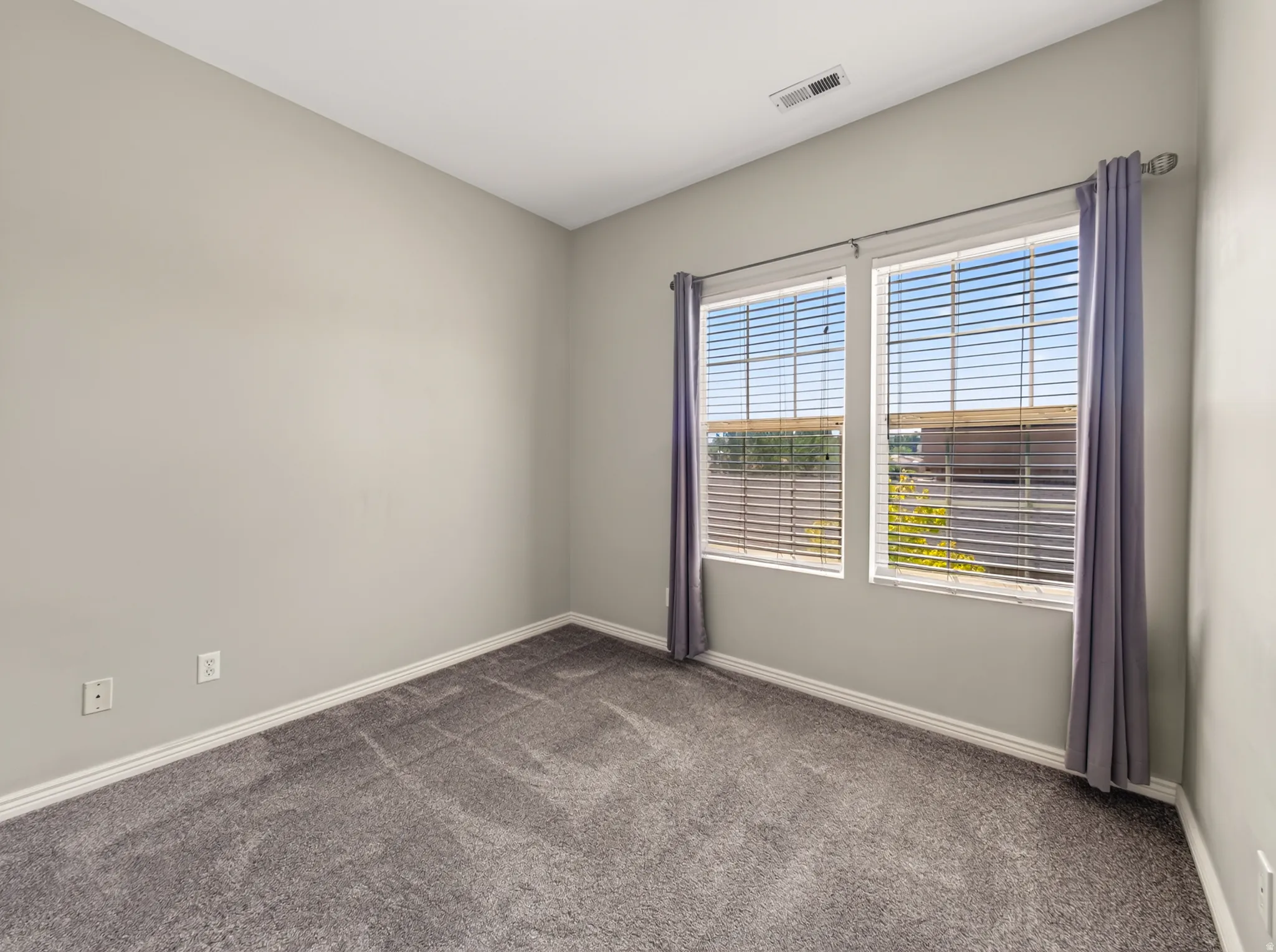 Bright bedroom offering neutral wall finishes, plush carpeting, and abundant natural light from dual glass doors with horizontal blinds and coordinating curtains