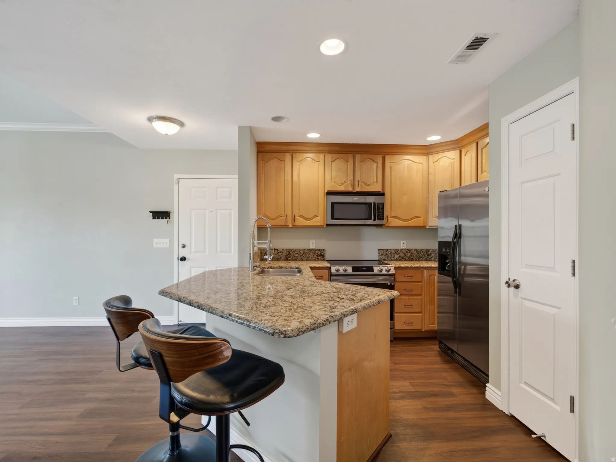 Kitchen featuring wood-finish flooring, granite countertops, wood cabinetry, stainless steel appliances, and an eat-at peninsula