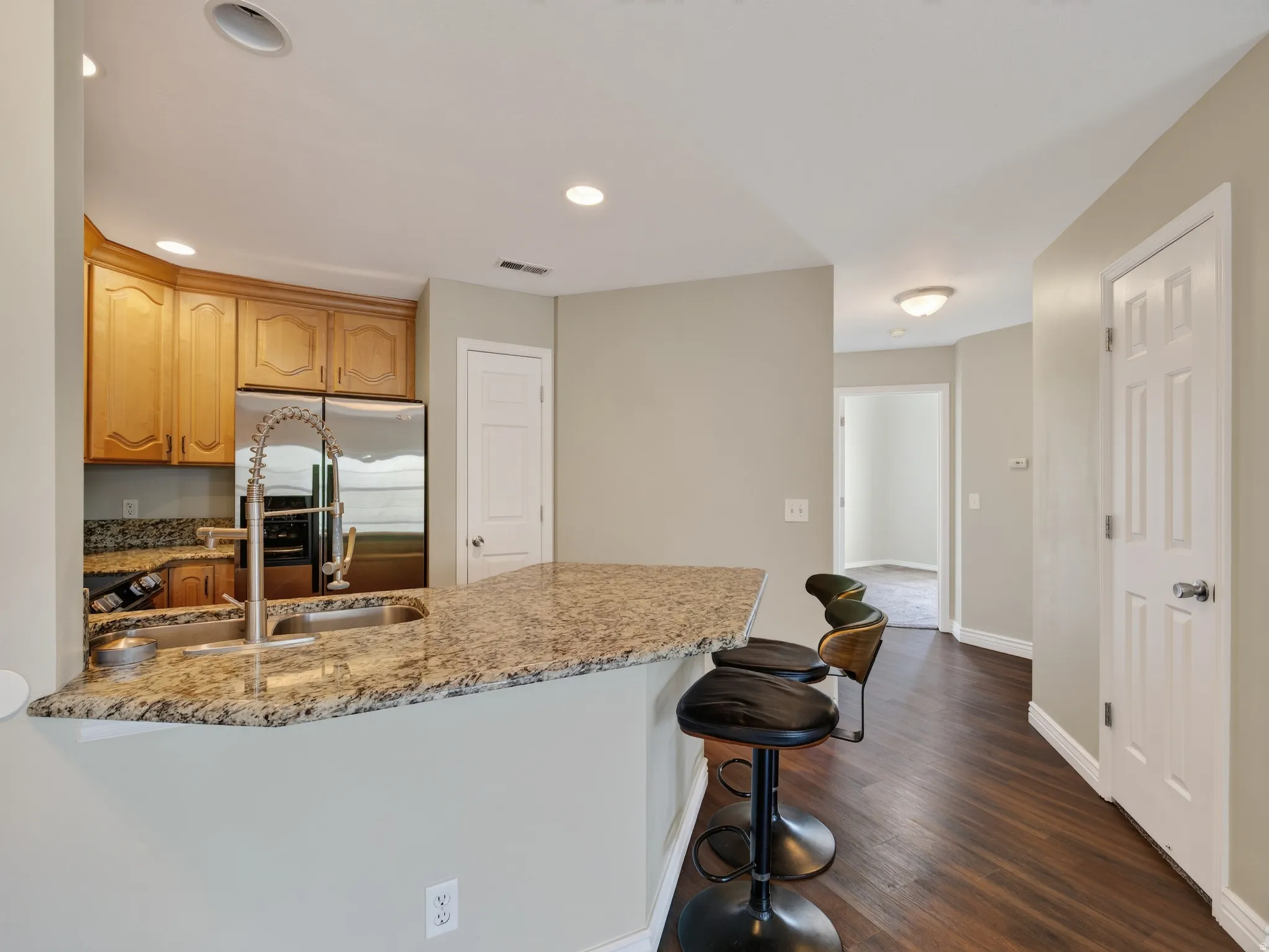 Kitchen featuring a breakfast bar with stone countertop, stainless steel sink with gooseneck faucet, light wood cabinetry, and stainless steel appliances