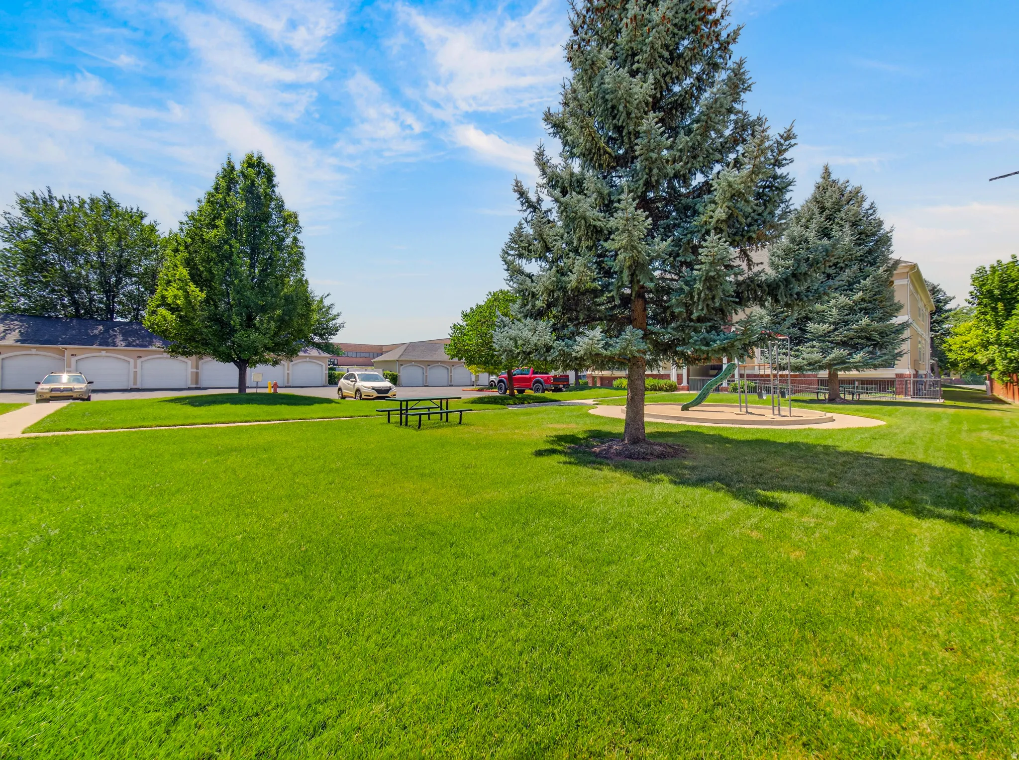 Expansive green space featuring a picnic area, mature trees, and a playground with a slide and climbing structure