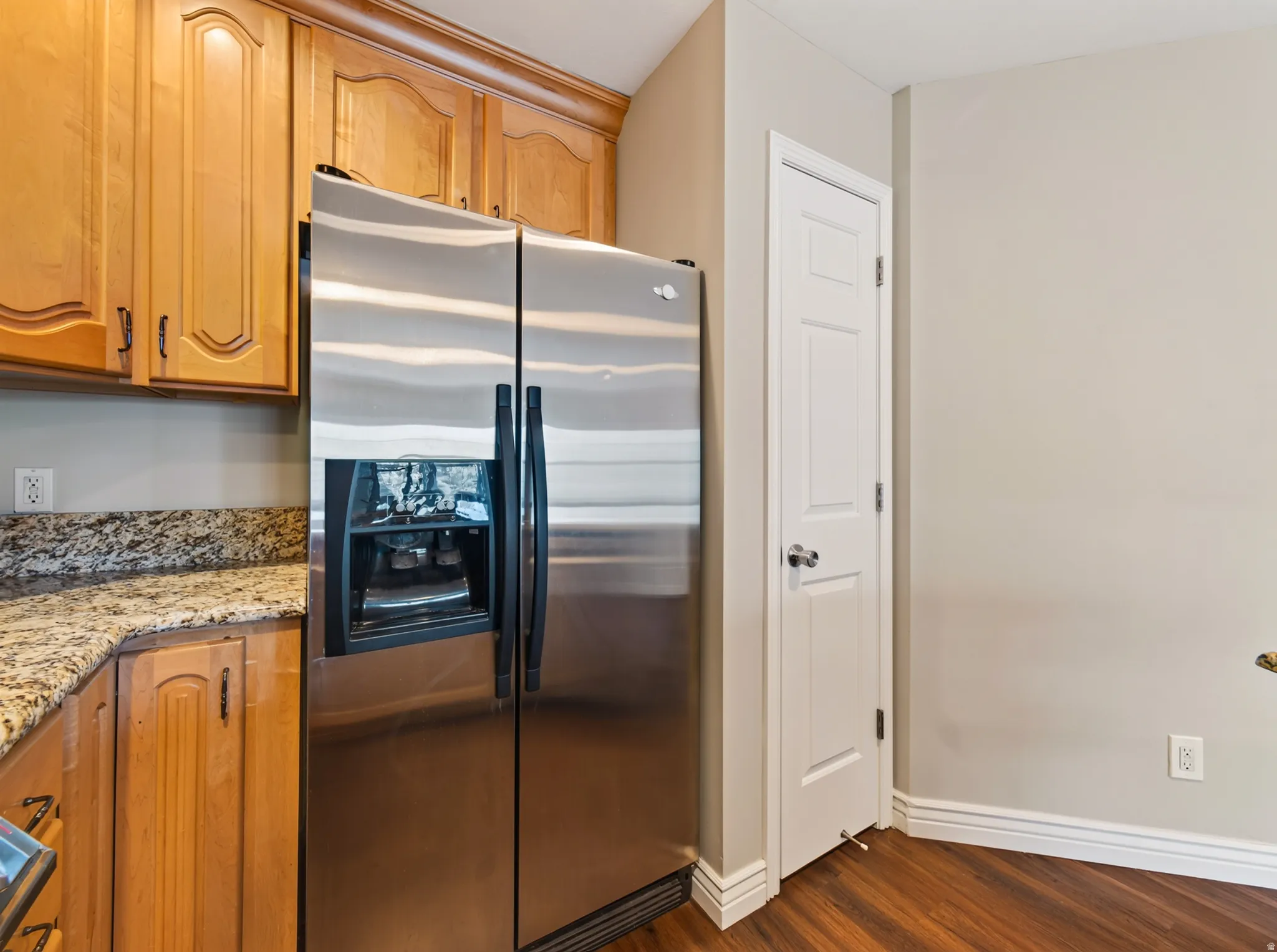 Stainless steel side-by-side refrigerator, wood-finish flooring, light-toned walls, white trim, and a white paneled door
