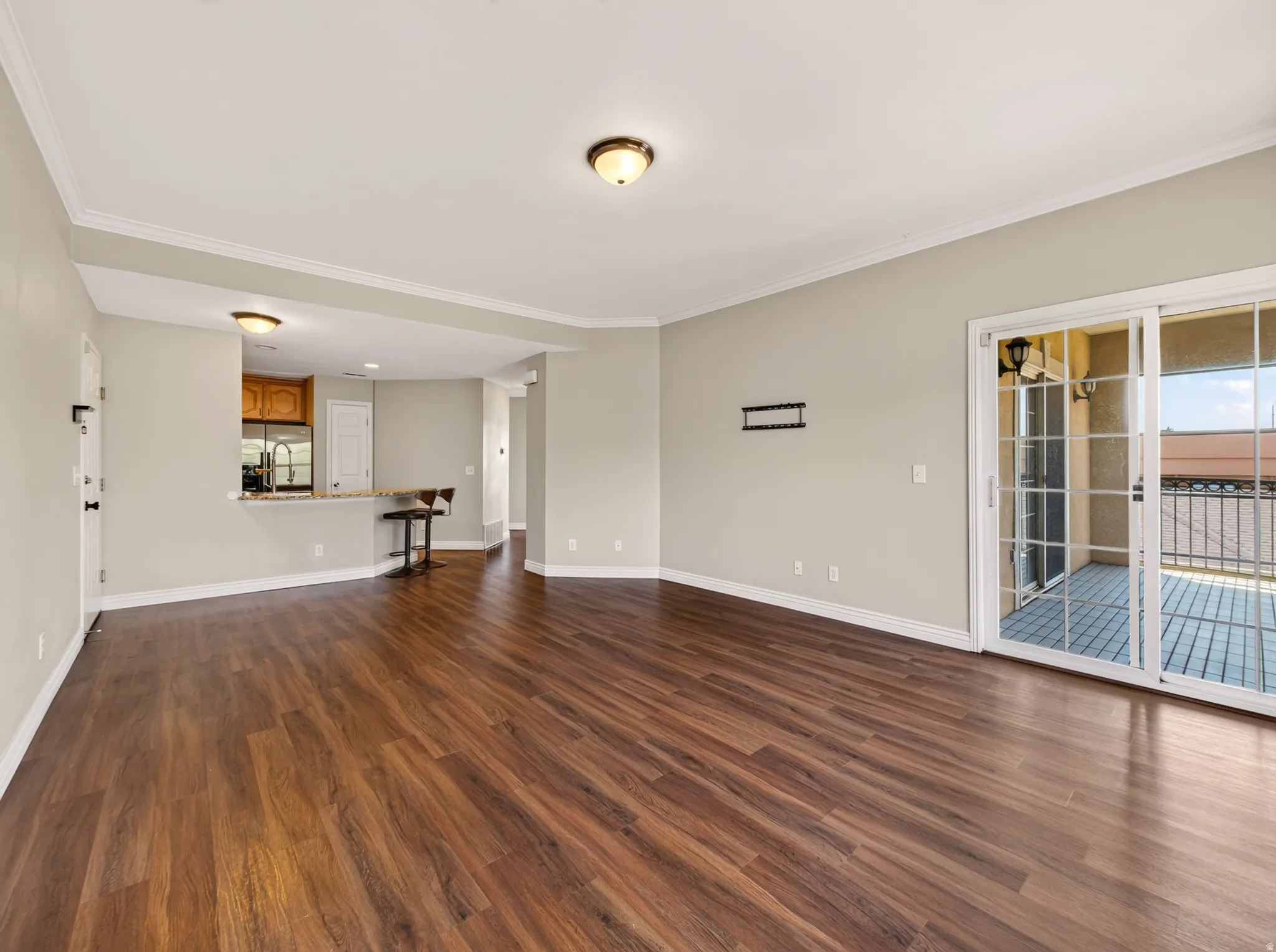 Spacious living area featuring wood-finish flooring, neutral wall tones, crown molding, and a sliding glass door opening to an outdoor balcony