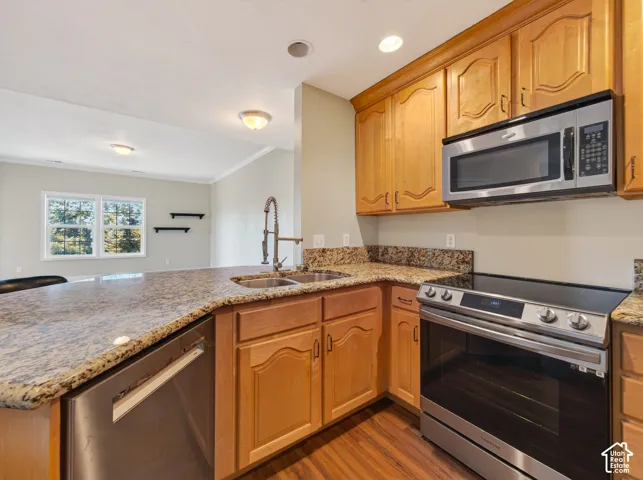 Kitchen featuring light wood cabinetry, granite-style countertops, stainless steel appliances, and wood-finish flooring