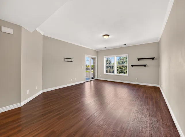 Spacious living area featuring rich wood-finish flooring, white crown molding, and neutral wall tones