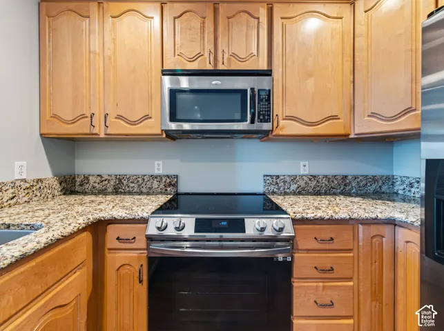 Kitchen featuring light wood cabinetry with arched panel doors, stone-finish countertops, stainless steel microwave, and a black glass-top range