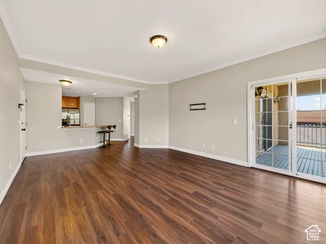 Spacious living area featuring wood-finish flooring, neutral wall tones, crown molding, and a sliding glass door opening to an outdoor balcony