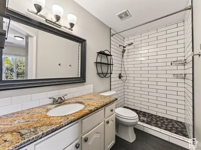 Bathroom featuring a granite-style countertop vanity with a white subway tile backsplash, a glass-enclosed shower with white subway tile walls, and a hexagonal tile shower floor