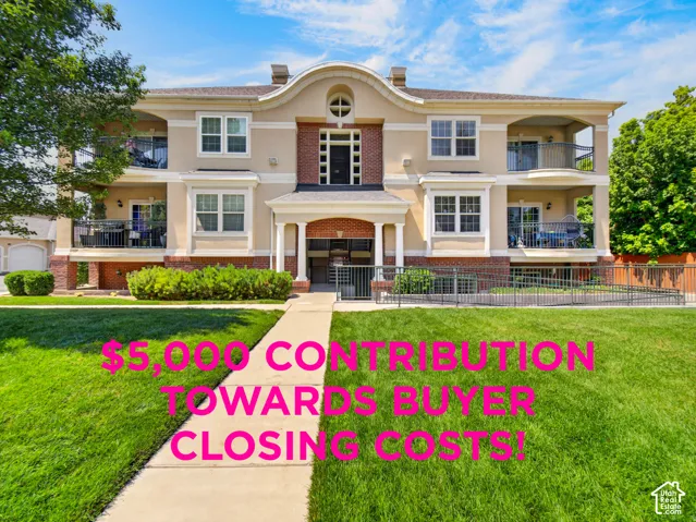 Stucco exterior with brick accents, arched entryway, multiple balconies with metal railings, accessible ramp entrance, and landscaped grounds