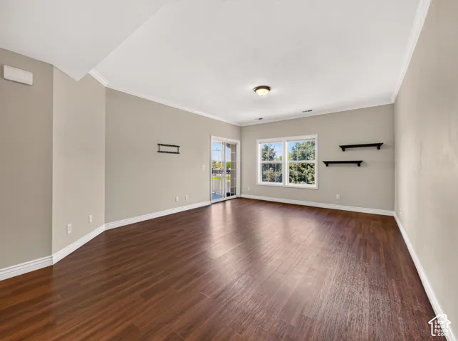 Spacious living area featuring rich wood-finish flooring, white crown molding, and neutral wall tones