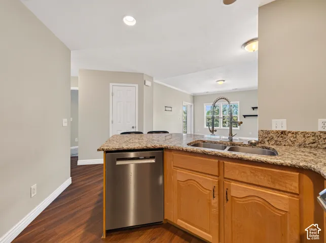 Kitchen island with a double basin sink and gooseneck faucet, light-toned wood cabinetry, granite countertops, and a stainless steel dishwasher