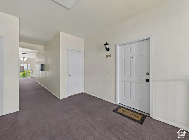 Entryway featuring a paneled door with a brass kickplate, a wall-mounted light fixture, and neutral-toned carpeting