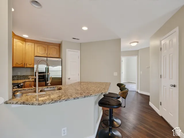 Kitchen featuring a breakfast bar with stone countertop, stainless steel sink with gooseneck faucet, light wood cabinetry, and stainless steel appliances