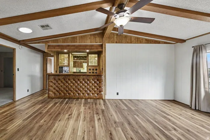 Living area featuring wood-finish flooring, exposed wood beams, and a built-in bar with tufted paneling and display cabinetry