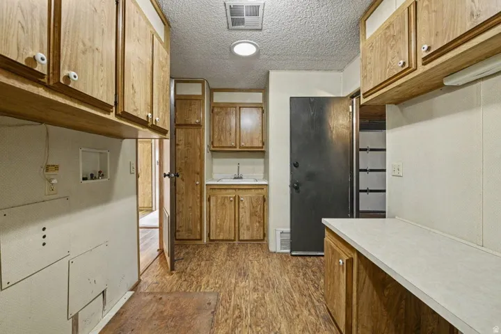 Utility room featuring wood-finish flooring, overhead cabinetry, a built-in sink with base cabinetry, a laundry hookup, and a built-in countertop