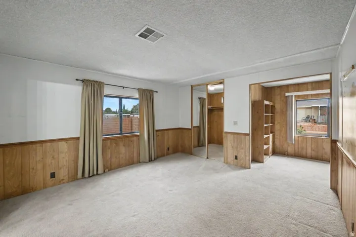 Carpeted room featuring wood paneling, multiple windows, built-in shelving, and a mirrored closet