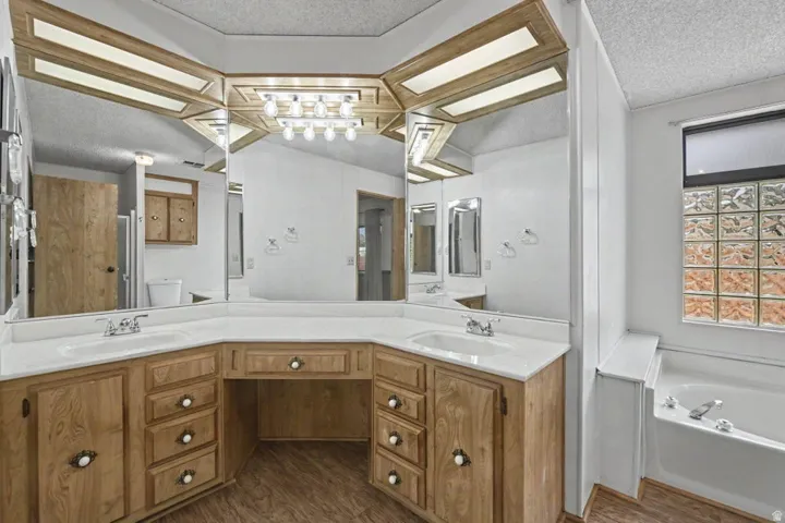 Expansive vanity area featuring dual sinks, integrated makeup station, wood-finish cabinetry, and a large wall-mounted mirror