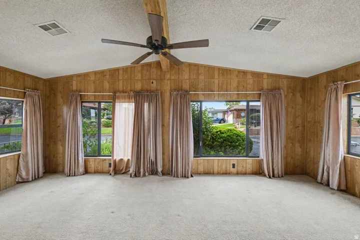 Room featuring wood-paneled walls, a vaulted ceiling with an exposed beam, and a ceiling fan