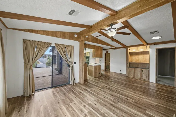 Spacious interior featuring wood-finish flooring, exposed beam ceiling with a ceiling fan, and a built-in entertainment center