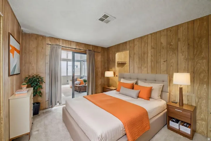 Room featuring wood paneling on all walls, soft carpet flooring, and a sliding glass door opening to an enclosed patio