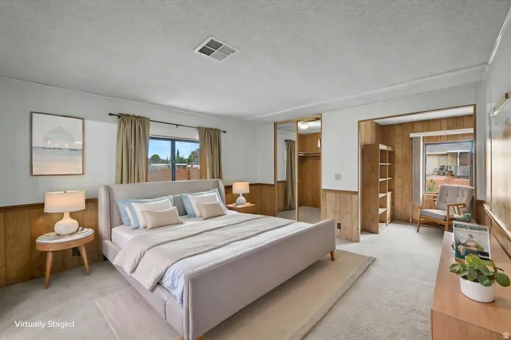 Carpeted bedroom featuring wood paneling, a large window, and built-in closet with mirrored sliding doors