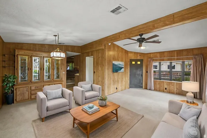 Living area featuring wood paneling throughout, a large picture window, and a ceiling fan with integrated lighting